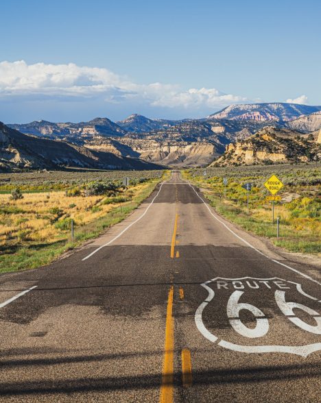 Scenic panoramic view of long straight road on famous Route 66 with historical street signs and paintings in classic american wild western mountain scenery in beautiful golden evening light at sunset